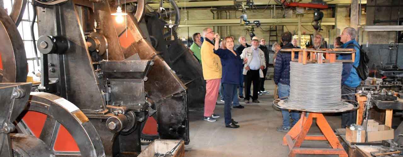 Gruppe von Menschen steht zwischen Maschinen der Nagelfabrik Wintherthur